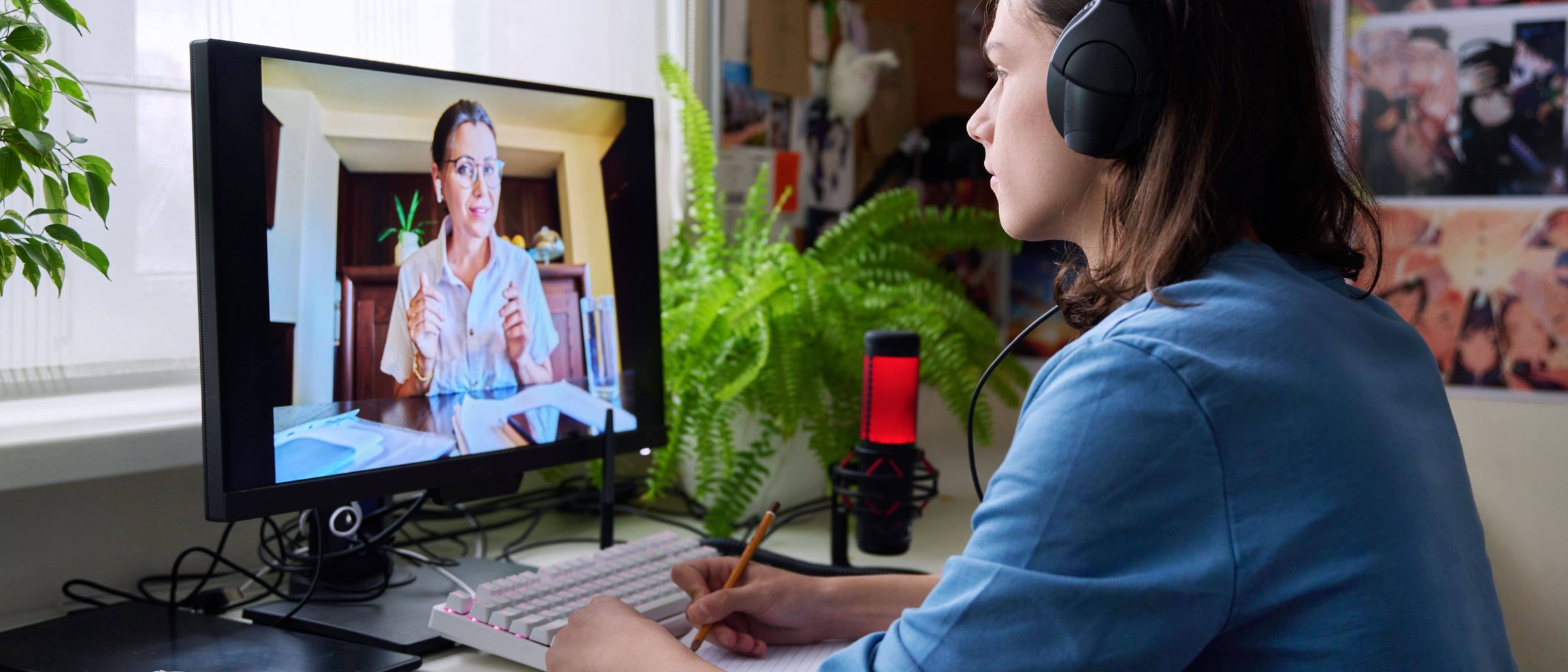 Woman with headphones watching online tutorial and taking notes at desk